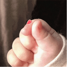 a close up of a person 's fist with a red heart on the thumb .