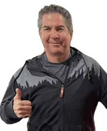 a man wearing a hoodie with trees on it giving a thumbs up