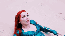 a woman with red hair and blue eyes is laying on the beach looking up at the sky .