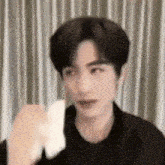 a young man in a black jacket is standing in front of a curtain and holding something in his hand .