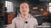 a man in a grey hoodie with a microphone around his neck is standing in a workshop ..
