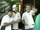 a group of men are standing next to each other in a room and one of them is wearing a white shirt with the letter b on it