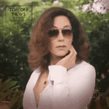 a woman wearing sunglasses and a white shirt is standing in front of a sign that says " torl on news "