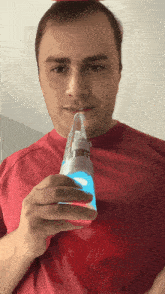 a man in a red shirt is holding a bottle with a light on it