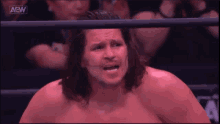a shirtless wrestler in a ring with the aew logo on the bottom left