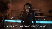 a man in a suit and mask is dancing in front of a fountain and says `` i happen to have some spare change ... ''