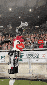 a chicken mascot stands in front of a banner that says mineiro sicoor