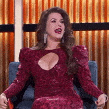 a woman in a red dress is sitting in a chair with her legs crossed and laughing .