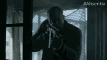 a man is holding a gun in front of a window with #absentia written on the bottom