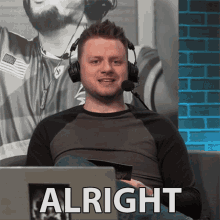 a man wearing headphones is sitting in front of a laptop and the word alright is on the screen