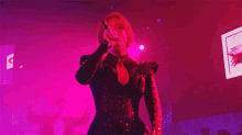 a woman singing into a microphone in front of a screen with a picture of an eye