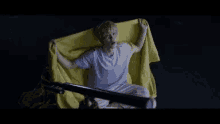 a young man is sitting on a bed holding a yellow blanket .