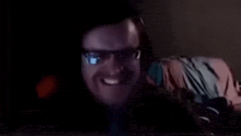 a man wearing glasses is smiling in front of a computer screen in a dark room .