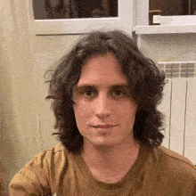 a young man with long curly hair is wearing a brown t-shirt .