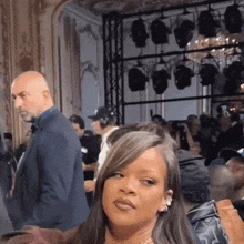 a woman with long hair is sitting in a room with a man in a suit standing behind her .