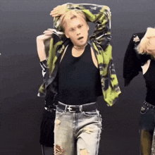 a man in a black tank top and ripped jeans is dancing in a group of people .
