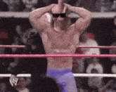 a wrestler wearing sunglasses is standing in a wrestling ring with his hands behind his head .