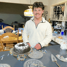 a young man stands in front of a cake with candles on it