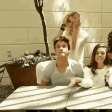 a group of people are sitting at a table and one of them is covering his face with his hands .