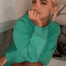 a woman in a green sweater is sitting on a table with her hand on her chin .