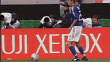 a soccer player kicking a ball in front of a fuji xerox banner