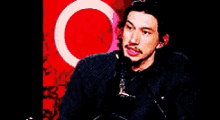 a man with a mustache is sitting in front of a red background with a circle in the middle .