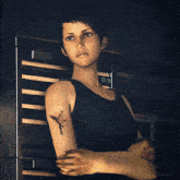a woman with a bird tattoo on her arm stands with her arms crossed