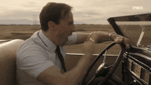 a man in a white shirt and tie is driving a car with the word max on the bottom