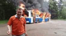 a man in an orange shirt stands in front of a burning bus