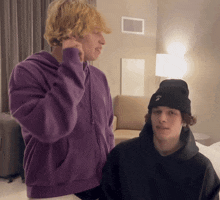 a man in a purple hoodie is talking on a cell phone next to another man in a black beanie
