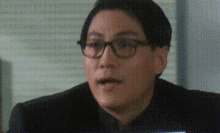 a man wearing glasses and a black suit is sitting in front of a computer .
