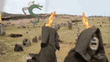 two people in hoods are standing in a field with flames coming out of their heads and a dragon in the background