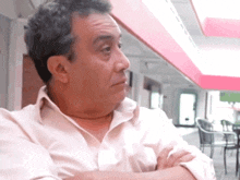 a man in a white shirt with his arms crossed looks to the side