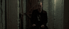 a young man in a black jacket is sitting in front of a wooden door .