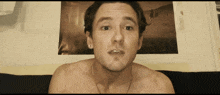 a man without a shirt is sitting in front of a picture on a wall