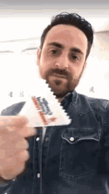 a man in a denim shirt is holding a piece of paper with a toothbrush on it .