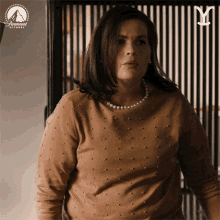 a woman wearing a brown sweater and pearls is standing in front of a paramount network logo