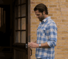 a man in a plaid shirt is standing in front of a brick building
