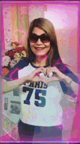 a woman wearing sunglasses and a shirt that says paris 75 makes a heart shape with her hands