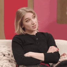a woman is sitting on a couch with her arms crossed and looking at the camera