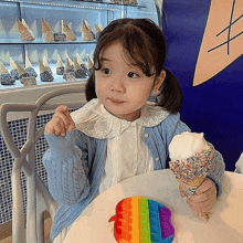 a little girl is sitting at a table holding an ice cream cone and a rainbow pop it toy .