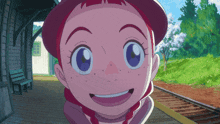 a girl with red hair and blue eyes is smiling in front of train tracks