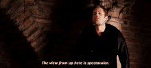 a man standing in front of a brick wall with the words " the view from up here is spectacular "