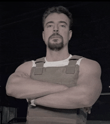 a man with his arms crossed and a beard is wearing a vest
