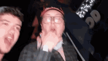 a man wearing glasses and a hat stands next to another man