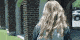 a woman with long blonde hair is standing in front of a brick building .