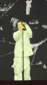 a man in a white suit is singing into a microphone on a stage .