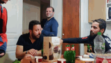 a group of men sitting around a table with a box that says ' supreme ' on it