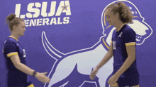 two girls shake hands in front of a lsua generals sign