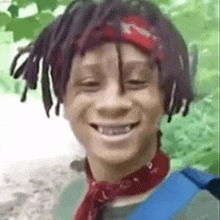 a young man with dreadlocks is smiling and wearing a bandana .